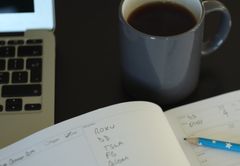 The Official Harvey Walsh Trading Journal open on a desk beside a laptop and a cup of coffee, with a day’s watchlist filled in